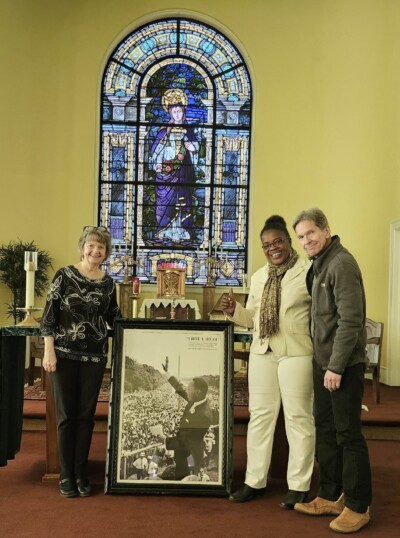 Three people are standing on an altar by a portrait of Martin Luther King