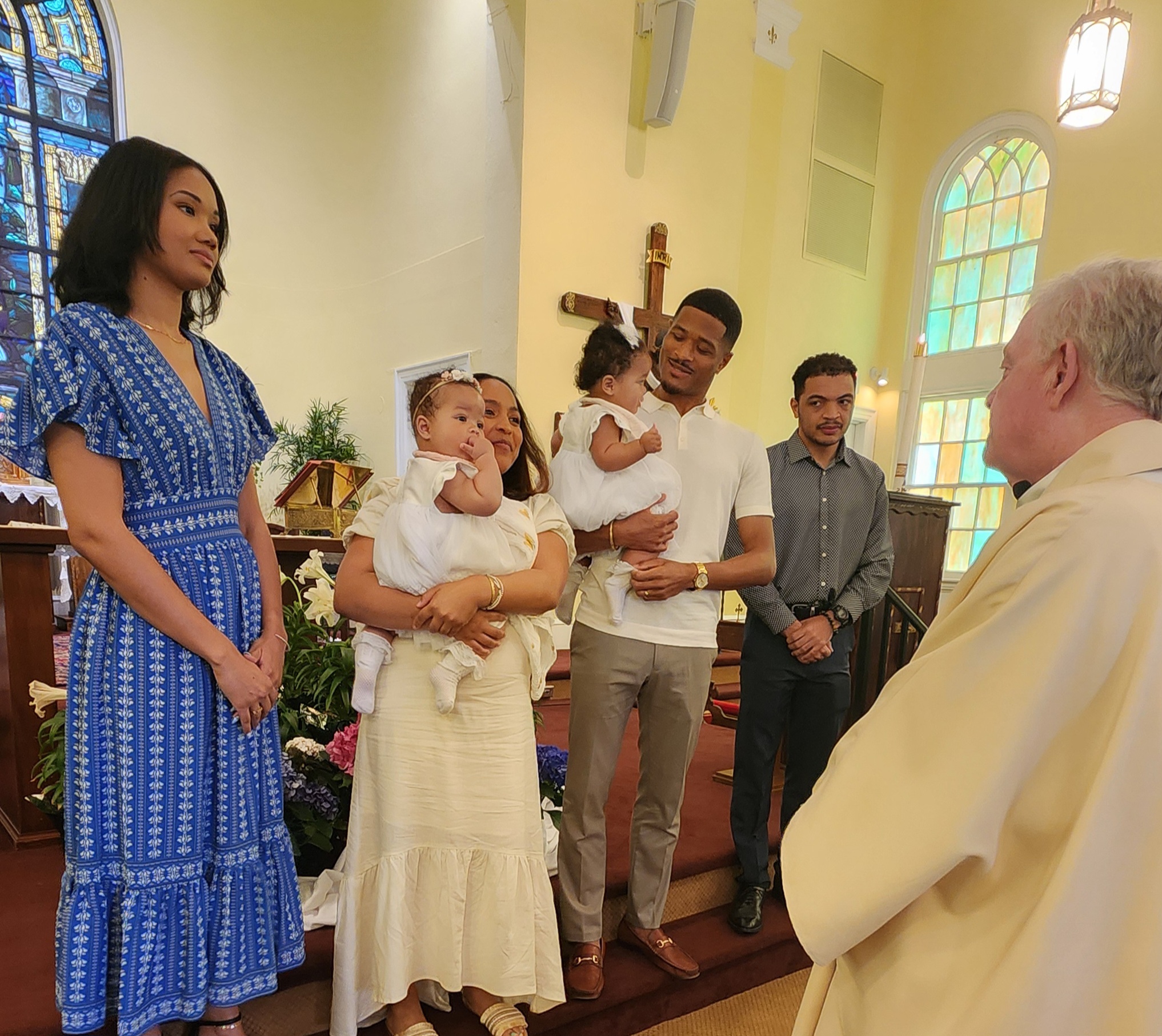 A couple is standing in front of the altar with their two babies, the priest and the babies godparents